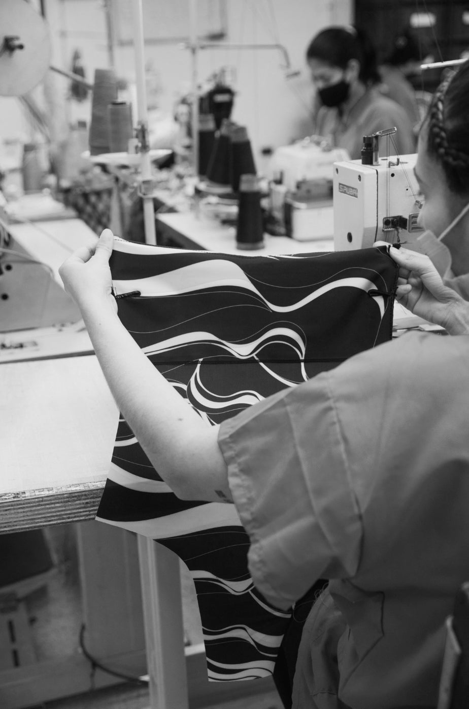 woman in a factory holding a Koraru one piece swimsuit in coral print