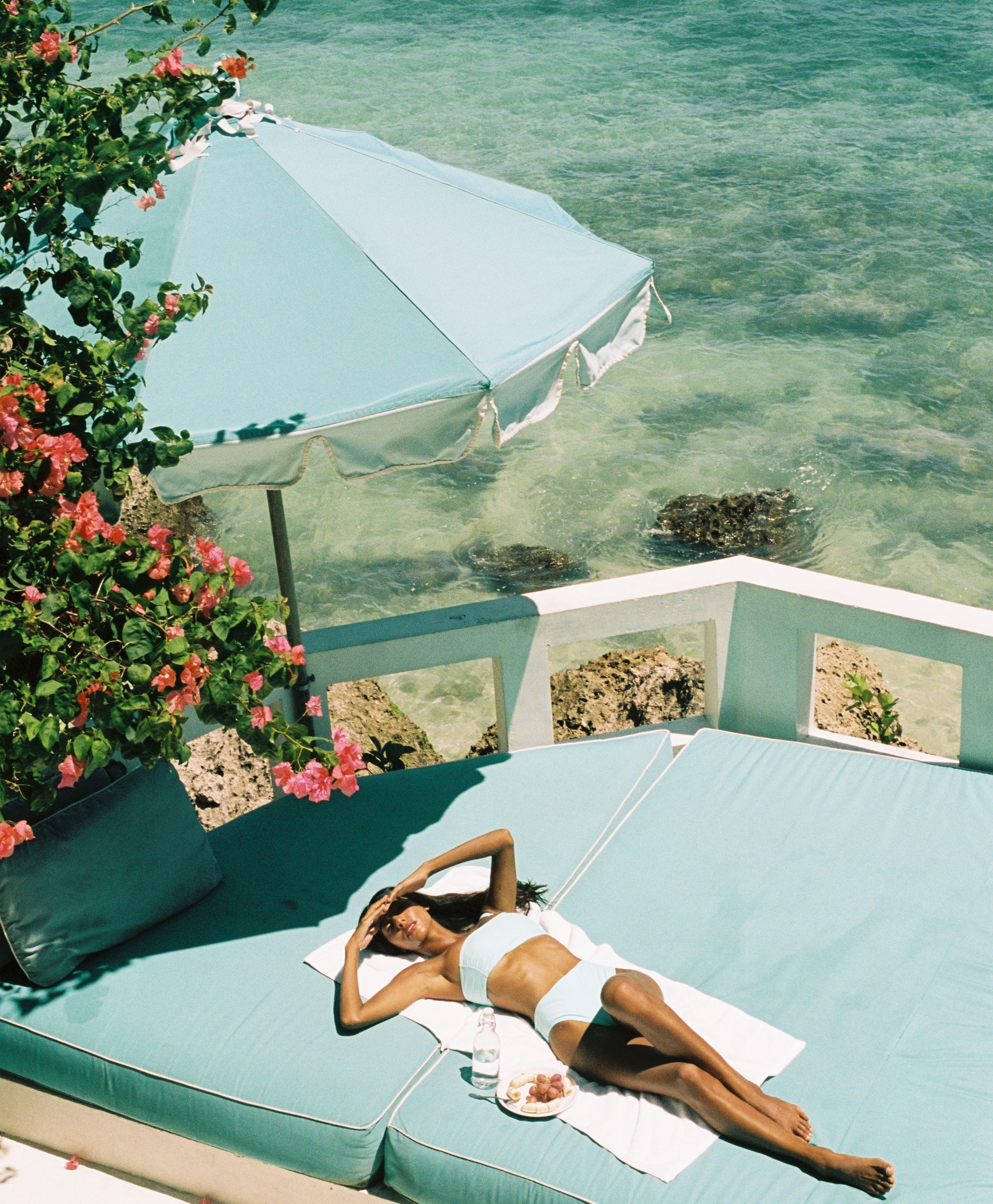 Woman lying on a sun lounger by the sea wearing a blue high waisted KORARU bikini